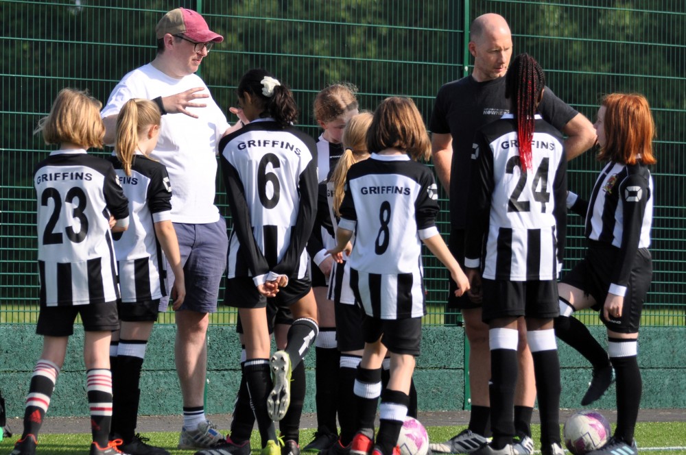 Group of junior girls in black and white kit listen to a coach talking